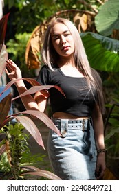 portrait of caucasian beauty girl ashen hair wear black t shirt and jean skirt standing in garden in high contrast day light - Shutterstock ID 2240849721