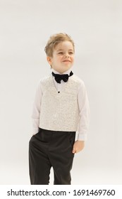 Portrait Of A Caucasian Boy 3-5 Years Old In A Classic Men 's White Shirt, Black Tie Butterfly And Vest Made Of Dressing Fabric. Child Smiles And Poses On White Background, Copyspace