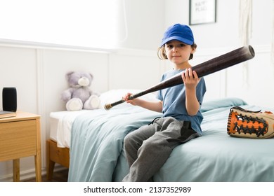 Portrait of a caucasian boy making eye contact while holding a baseball bat in his bedroom and ready to go to practice 