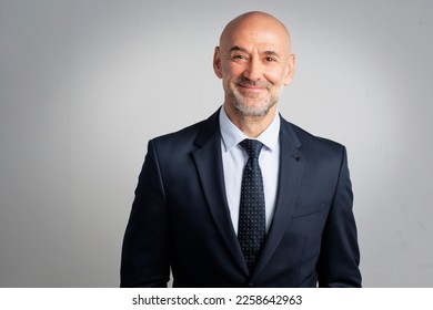 Portrait of caucasian business man looking at camera and smiling. Confident mature male professional is in suit. He is against gray background.