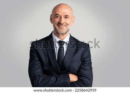 Portrait of caucasian business man looking at camera and smiling. Confident mature male professional is in suit. He is against gray background.