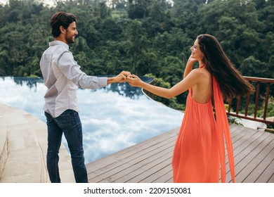 Portrait of caucasian couple dancing near swimming pool. Young man and woman enjoying at poolside of a holiday resort in nature. - Powered by Shutterstock