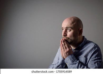Portrait of caucasian depressed sad bald man in grey shirt on grey background. Side profile view. Prayer position
