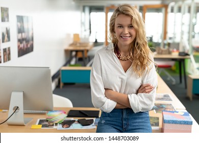 Portrait of Caucasian female graphic designer with arms crossed sitting at desk in a modern office. This is a casual creative start-up business office for a diverse team