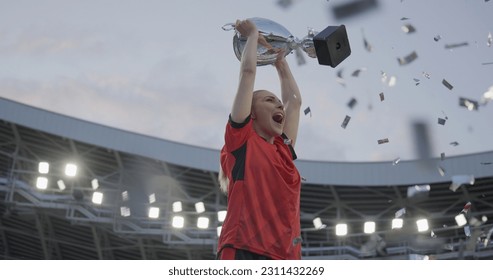 Portrait of Caucasian female soccer football player celebrating victory in the championship, lifting the trophy above her head in a huge stadium - Powered by Shutterstock