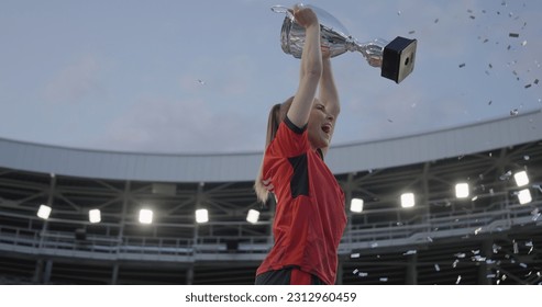 Portrait of Caucasian female soccer football player celebrating victory in the championship, lifting the trophy above her head in a huge stadium - Powered by Shutterstock