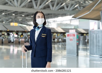 Portrait Of Caucasian Flight Attendant Standing In Airport Terminal. Attractive Beautiful Cabin Crew Or Air Hostess Woman Wearing Face Mask Prepare To Work In Airplane During Covid19 Pandemic Crisis.