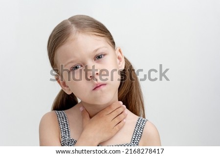 Portrait of caucasian little girl of 6 years holding hand on throat showing difficulty in speaking or sore throat. Concept dysarthria