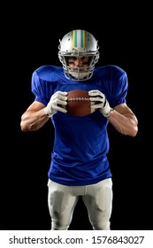 Portrait Of A Caucasian Male American Football Player Wearing A Team Uniform, Pads And A Helmet, Stripes Of Eye Black Under His Eyes, Holding A Football In Two Hands. Vertical Shot