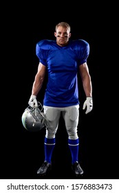 Portrait Of A Caucasian Male American Football Player Wearing A Team Uniform, Pads, Gloves And Eye Black Under His Eyes, Holding A Helmet