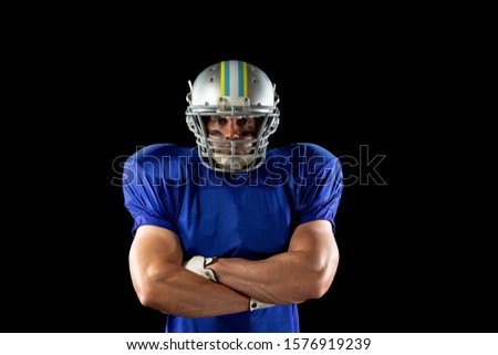 Portrait of a Caucasian male American football player wearing a team uniform, pads and a helmet, standing with arms crossed and eye black under his eyes