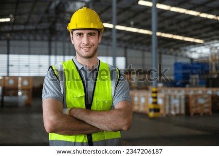 Portrait of caucasian male factory worker looking at camera with his arms crossed confidently in the process of working in warehouse.