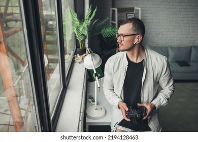 Portrait Of Caucasian Male Photographer Looking Away And Keeping Camera In Arms While Standing In Office. Snapshot, Portrait, Photographer, Hobby.