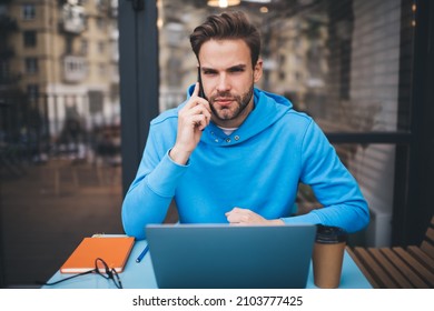 Portrait of Caucasian male receive international call during remote working in street cafe, skilled IT professional with laptop computer looking at camera during roaming mobile communication