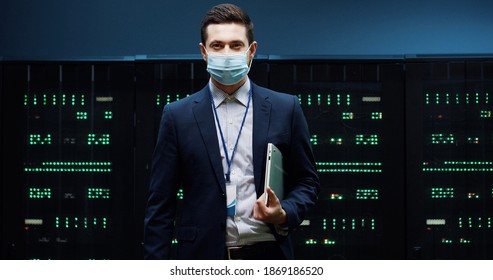 Portrait of Caucasian male security engineer in mask standing in datacenter checking security of processors network with digital information. Handsome man work in big data storage Technologies concept