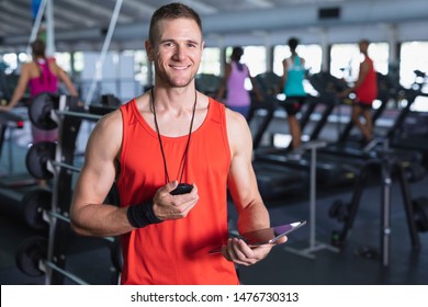 Portrait of Caucasian male trainer using digital tablet in fitness center. Bright modern gym with fit healthy people working out and training - Powered by Shutterstock