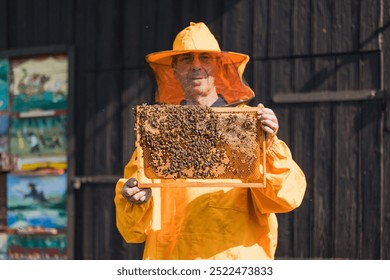 Portrait of a Caucasian man, beekeeper in yellow protective gear holding a hive frame covered with comb and bees - Powered by Shutterstock