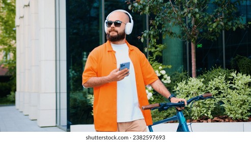 Portrait caucasian man going near business centre carrying bicycle using smartphone. Portrait of confident young male in stylish casual clothes with modern bike on city street. - Powered by Shutterstock