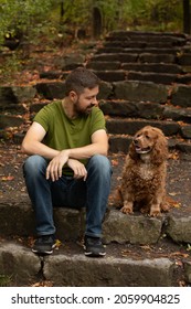 Portrait Of A Caucasian Man And His Cocker Spaniel Dog Sitting On Cement Stairs.