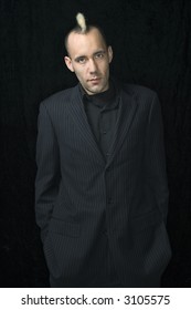 Portrait Of Caucasian Man In Suit With Mohawk Against Black Background.