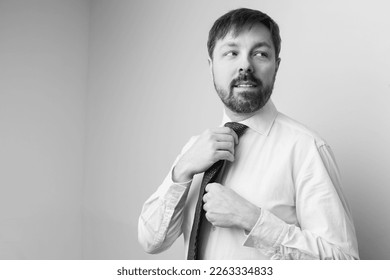 Portrait of a caucasian man wearing a white button up shirt and a tie. He is adjusting his tie. This photo is black and white. - Powered by Shutterstock