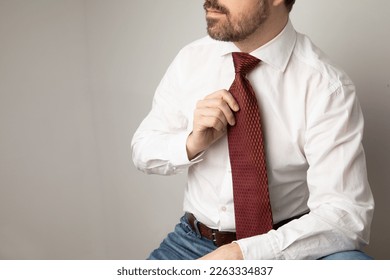 Portrait of a caucasian man wearing a white button up shirt and a red tie. He is adjusting his tie.  - Powered by Shutterstock