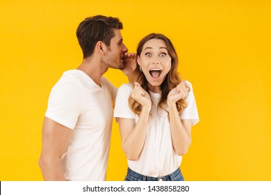 Portrait Of Caucasian Man Whispering Secret Or Interesting Gossip To Excited Woman In Her Ear Isolated Over Yellow Background