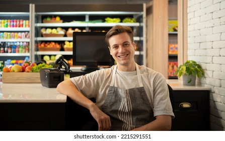 Portrait Of A Caucasian Man Working On Cashier In A Supermarket Or Retail Shop, Snacks And Food On Grocery Products Shelves. Food Shopping. People Lifestyle. Checkout Business Counter Service. Worker