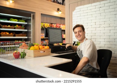 Portrait Of A Caucasian Man Working On Cashier In A Supermarket Or Retail Shop, Snacks And Food On Grocery Products Shelves. Food Shopping. People Lifestyle. Checkout Business Counter Service. Worker