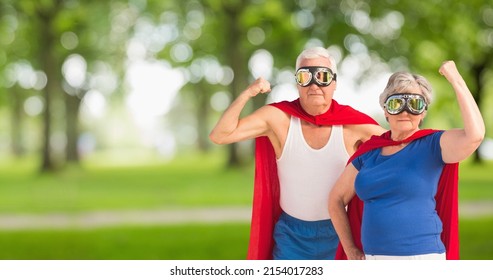 Portrait Of Caucasian Senior Couple Wearing Red Capes And Masks Flexing Muscle Against Trees In Park. Love, Togetherness, Superhero, Power, Fantasy, Unaltered, Senior Citizens, Retirement, Awareness.