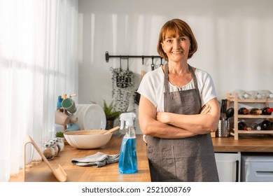 Portrait of Caucasian senior elderly woman cleaning kitchen at home. Attractive mature old housekeeper cleaner smiling, looking at camera while wiping dining table for housekeeping housework or chores - Powered by Shutterstock