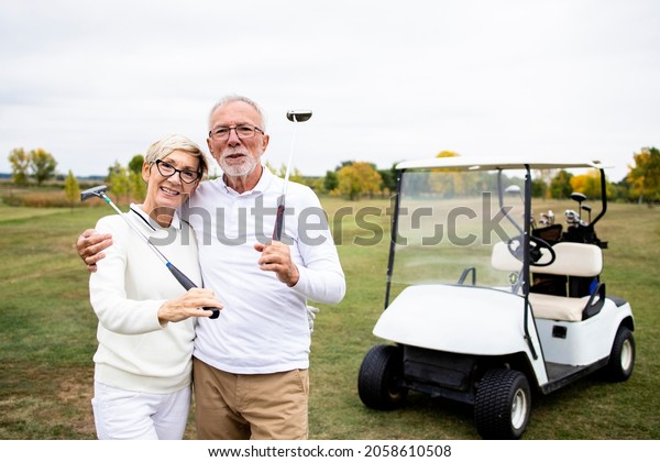 Portrait of caucasian senior golfers with golf\
clubs standing on the golf\
course.