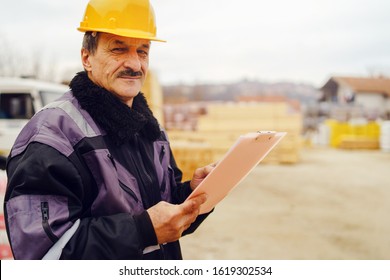 Portrait Of Caucasian Senior Man Construction Worker General Laborer Building Contractor Wearing Yellow Protective Helmet Holding Pen And Document Checking Data Report Project On The Site