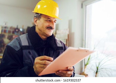 Portrait Of Caucasian Senior Man Construction Worker General Laborer Building Contractor Wearing Yellow Protective Helmet Holding Pen And Document Checking Data Report Project In The Office Warehouse