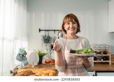 Portrait of Caucasian senior woman hold a bowl of vegetables in house. Attractive mature elderly older wear apron, spend leisure time cook foods for health care in house. Diet and Healthy food concept - Powered by Shutterstock