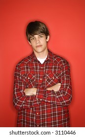 Portrait Of Caucasian Teen Boy With Arms Crossed Standing Against Red Background Wearing Flannel Shirt.