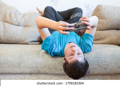Portrait of Caucasian teenager with large smartphone or game console in hands, playing or engaging over social media while lying his back on a sofa - Powered by Shutterstock