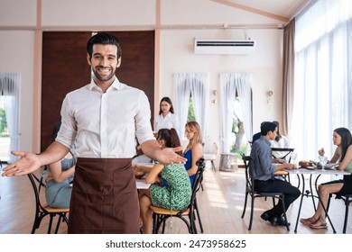 Portrait of Caucasian waiter standing and look at camera in restaurant. Attractive server service man working by receiving order serve from customer at table in dining room at cafeteria with happiness - Powered by Shutterstock