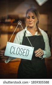 Portrait of a Caucasian woman with a black apron,  standing behind a glass door with the sign ''closed''