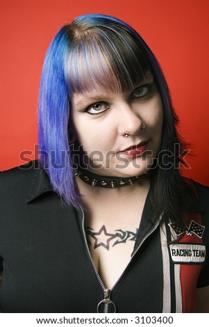 Portrait of Caucasian woman with blue hair, tattoo, and spike collar against orange background.