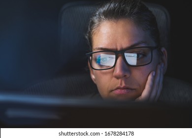 Portrait of a Caucasian woman with glasses sitting and watching a computer screen