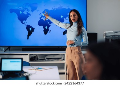 Portrait of a caucasian woman team leader speaking at office brainstorming while pointing on a big screen with a graphic of a world map a sales points. Female boss holding a meeting in an office. - Powered by Shutterstock