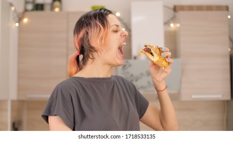 Portrait Of Caucasian Young Beautiful Woman Greedily Eagerly Eating Food During Quarantine Due To Coronavirus. Charming Happy Hungry Woman On Diet Laugh And Biting Off Big Meat Pie. Close Up.