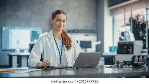 Portrait of Caucasian Young Female Scientist Using Laptop Computer, Looking at Camera and Smiling in a Laboratory. Confident Professional Woman Working as Lead Engineer, Monitoring Technology Projects - Powered by Shutterstock