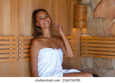 Portrait of caucasian young woman in a bathrobe smiling while relaxing in the sauna. Spa, wellness and relaxation concept