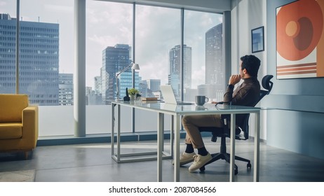 Portrait of Charismatic Arab Businessman Sitting at His Desk Working on Laptop Computer in Big City Office. Successful Digital Entrepreneur Doing Data Analysis for e-Commerce Startup.