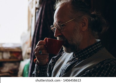 a portrait of a charismatic, wise and talented artist who sits in his small studio filled with paintings, paints and canvases and drinking tea or coffee. selective focus, noise effect