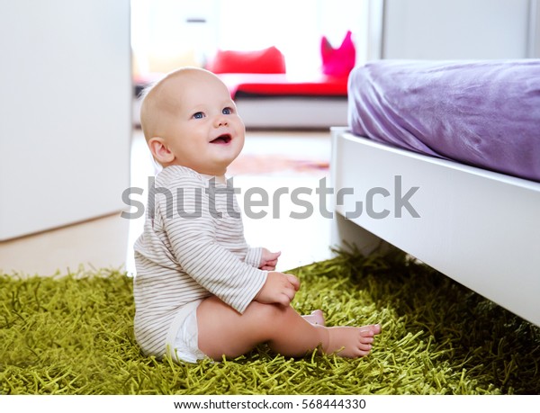 家の中に住む魅力的な8 9ヶ月の赤ちゃんのポートレート 好奇心に満ちた笑顔の子どもが 周りの世界を探検します 床に座っているかわいい赤ちゃん の写真素材 今すぐ編集