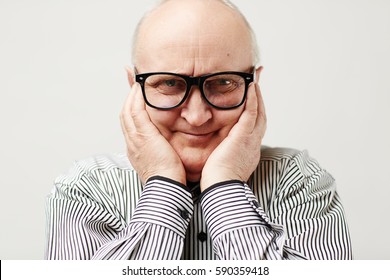 Portrait Of Charming Aged Man In Eyeglasses And Striped Shirt Making Funny Face By Squishing Cheeks With His Hands