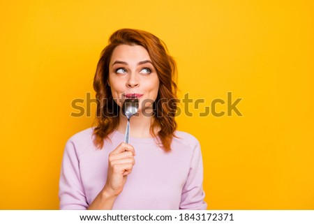 Portrait of charming beautiful cute inspired positive woman hold lick spoon think thoughts about yummy breakfast look copyspace wear pink jumper isolated over yellow color background